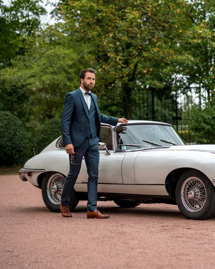 Costume Camilliano Sandillon bleu, trois pièces, en pied devant une voiture de collection